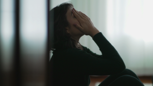 Depressed woman sitting on floor covering face with hands in despair