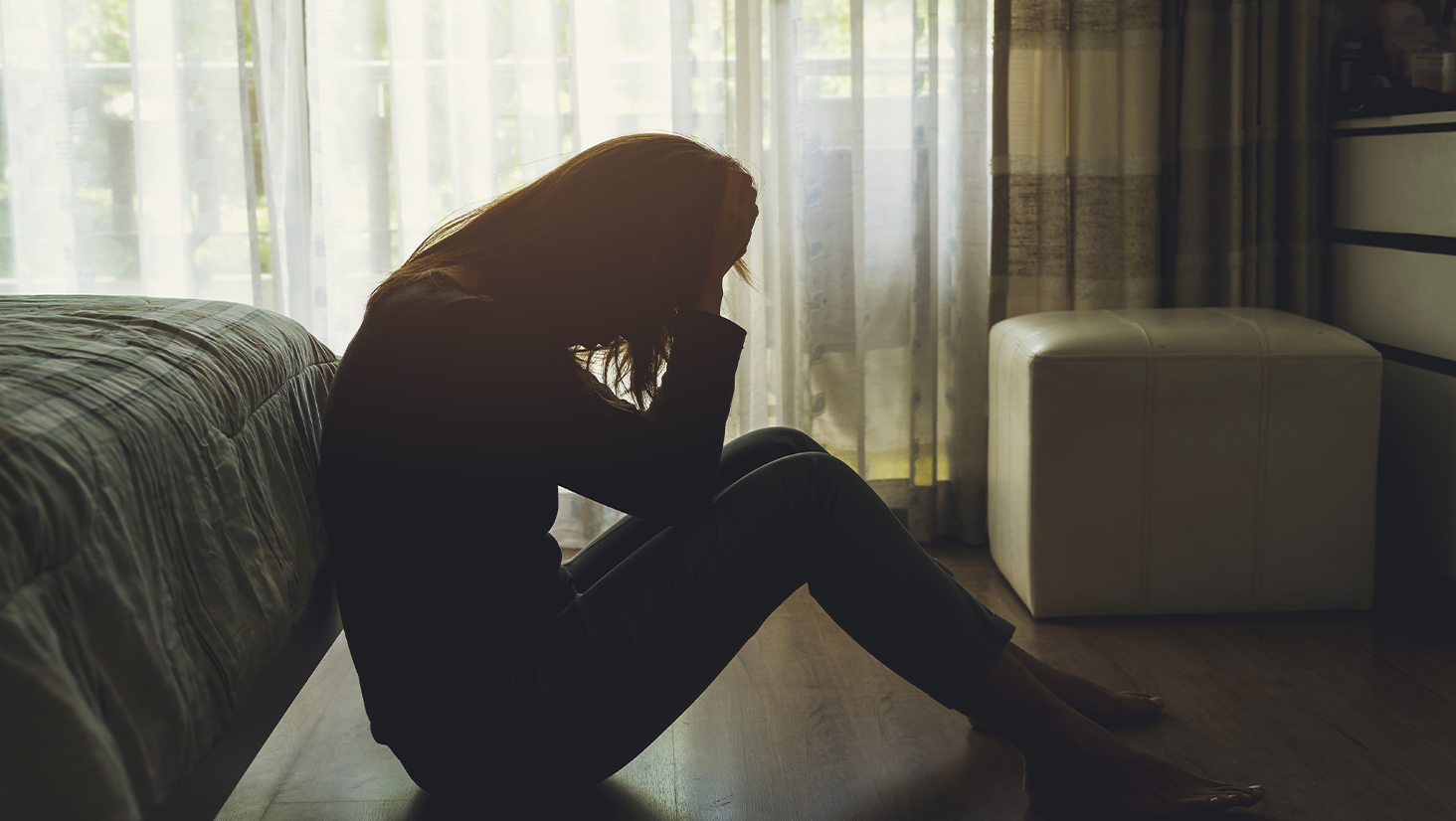 depressed woman sitting head in hands in the dark bedroom