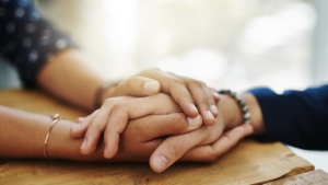 Holding hands, support and closeup with trust, solidarity and community on a home table. Therapy, diversity and gratitude of friends together with hope, respect and love for grief empathy and forgive.